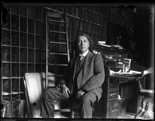 Titre original :  Glass negative (black and white); portrait of John Ojijatekha Brant-Sero, a Mohawk loyalist, seated inside a study, wearing a three piece suit; bookcases, a desk, a ladder and a chair are behind him; Canada.  Photographic process